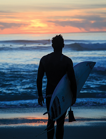 a surfer walking towards the ocean at sunrise