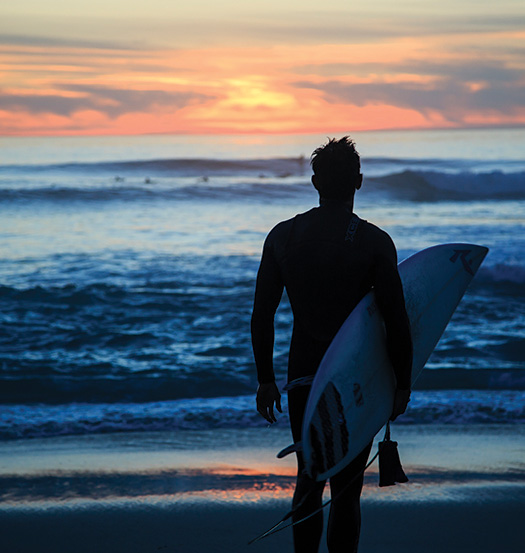 a surfer walking towards the ocean at sunrise