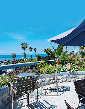 patio area with two person tables and an umbrella overlooking the ocean in the distance