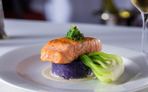 a gourmet salmon dish on a white dish next to a glass of white wine