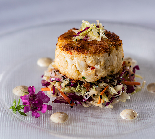 crab cake under a bed of cole slaw garnished with sauce and flowers