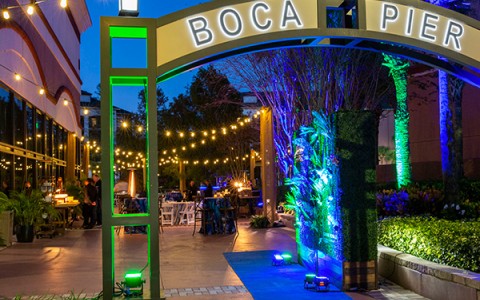 boca pier sign at night with a view of string lights hung behind it 
