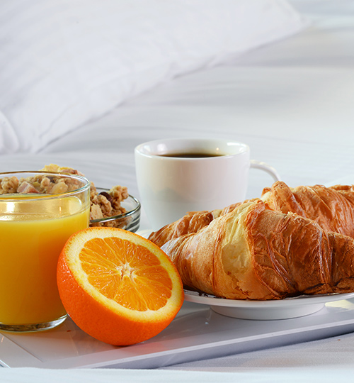 close up of breakfast including orange juice an orange croissants and a cup of coffee