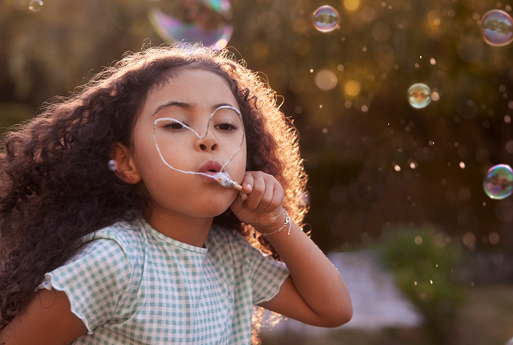 little girl blowing bubbles with bubbles surrounding her