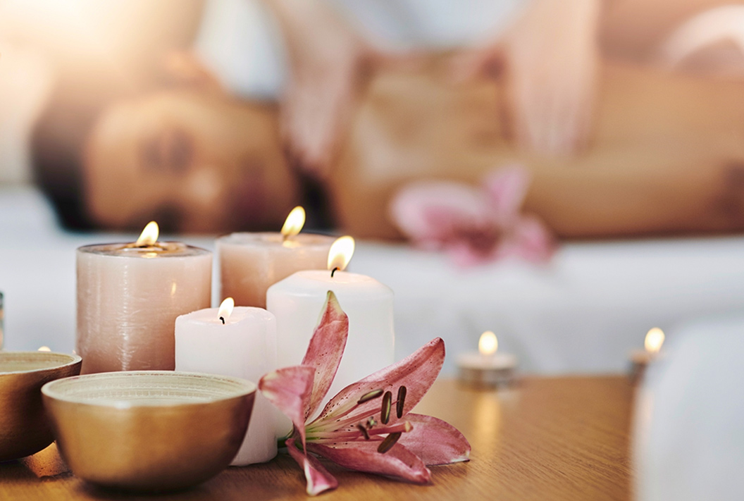 focus on candles and flower while woman gets massage in the background