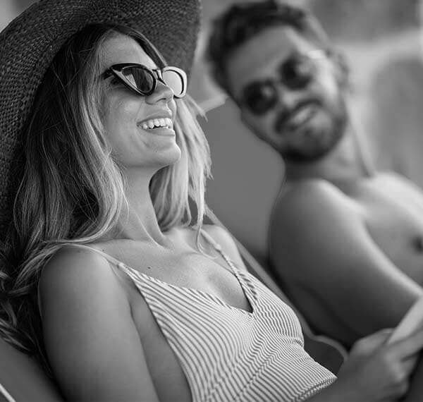 black and white photo of a girl with sunglasses, smiling and a boy looking at her