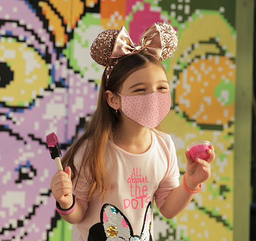 girl with golden mickey mouse ears, holding pink paint and a paintbrush in a Disney park activity