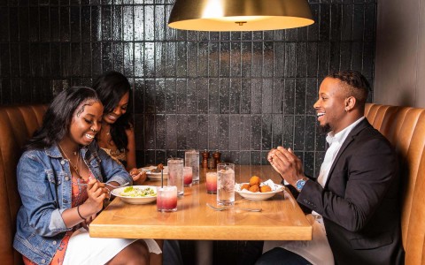 2 women and 1 man sitting in a booth eating together while smiling