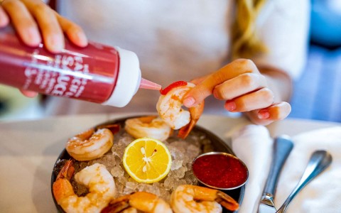 hands picking up shrimp on ice and adding sauce to the shrimp