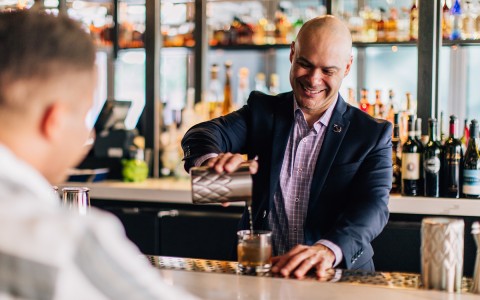 bar tender pouring customer a drink with full bar behind him
