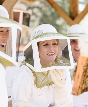 Three young woman wearing beekeeping clothes smiling looking at bee panel