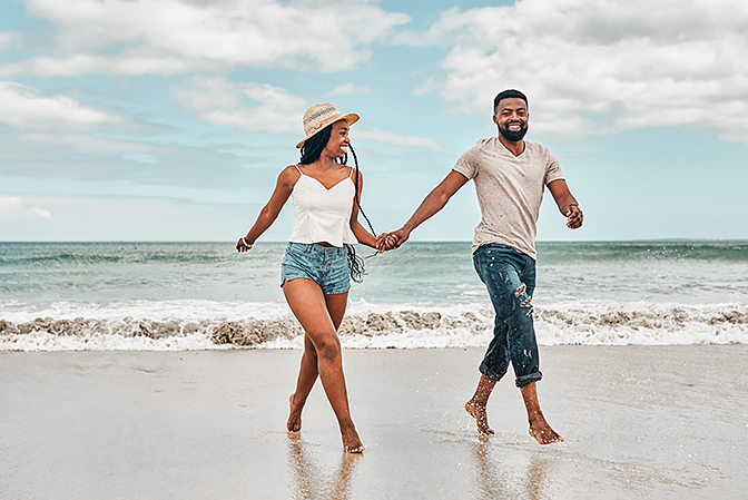 man and woman holding hands while walking on the beach