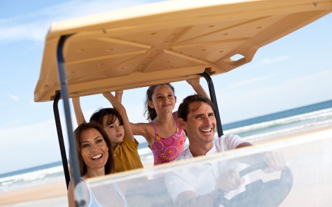 A happy family on a Golf Rental card at the beach