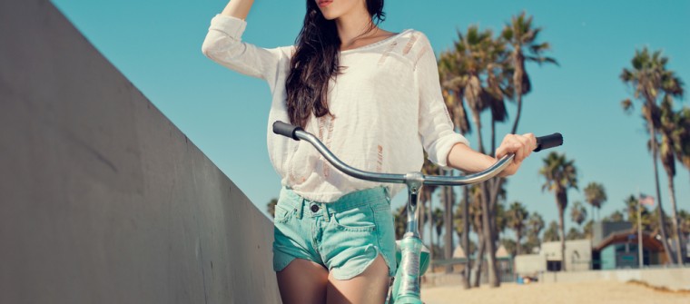 young woman with sunglasses by a sunny beach with a bike