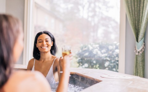 two women toasting their glasses while relaxing in the hot tub
