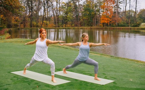 two women doing yoga on mats outside by the water
