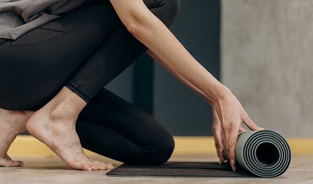 woman with black leggings unrolling her yoga mat