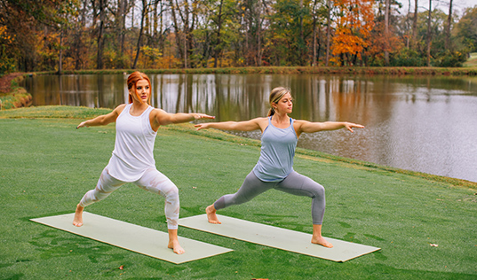 two ladies doing yoga by the pond