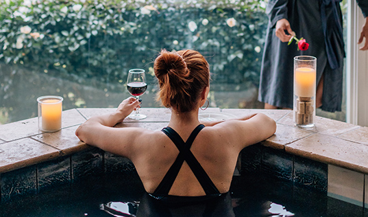 woman in hot tub with glass of wine and candles
