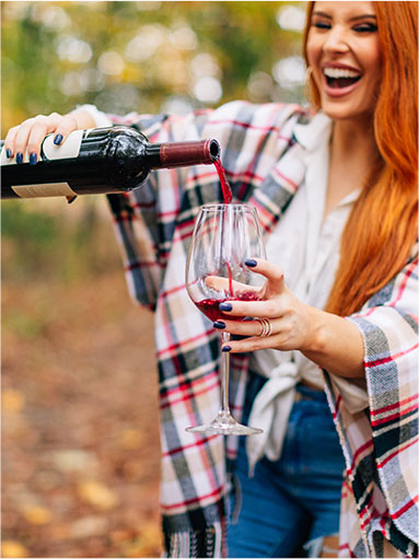 woman with bright orange hair pouring some wine into a glass