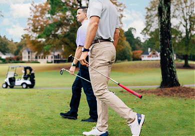 Two men walking on golf course with golf clubs in hand.