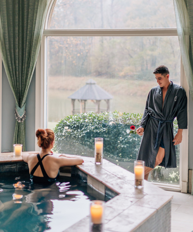 woman in swim suit sitting in the hot tub talking to a man standing close by in a grey bathrobe
