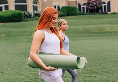 two women holding yoga mats and walking outside