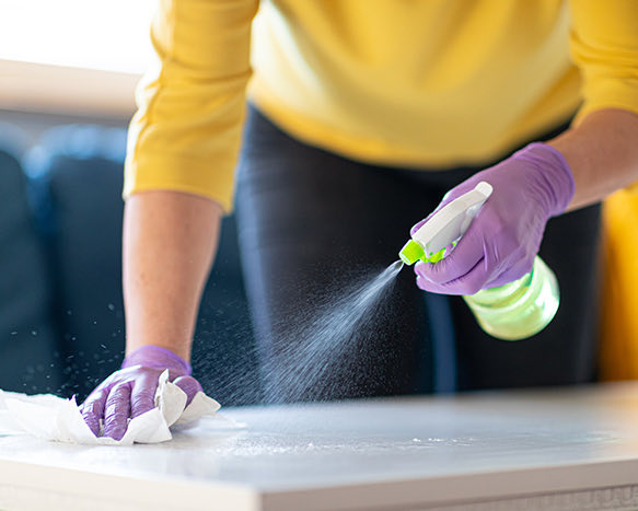 person in gloves spraying disinfectant and wiping the counter