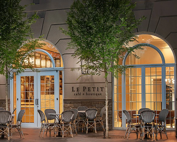 exterior of le petite cafe in the evening with a couple of trees and outside seating in groups of four