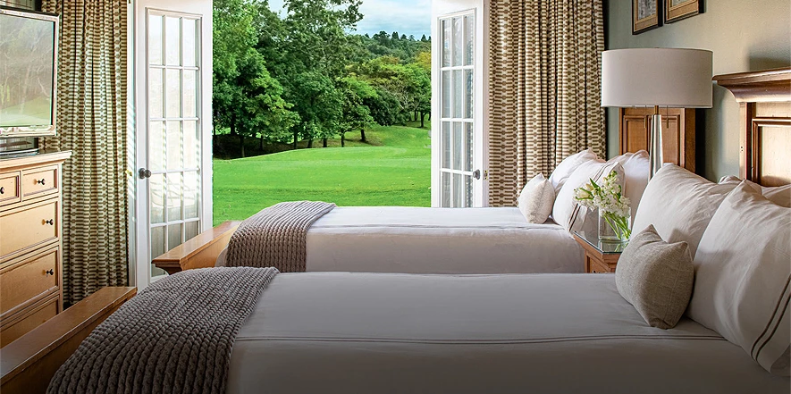 two beds in a room with open french doors looking out over a golf course