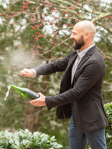 man popping a bottle of champagne outside