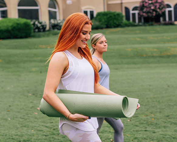 two women walking outside holding yoga mats