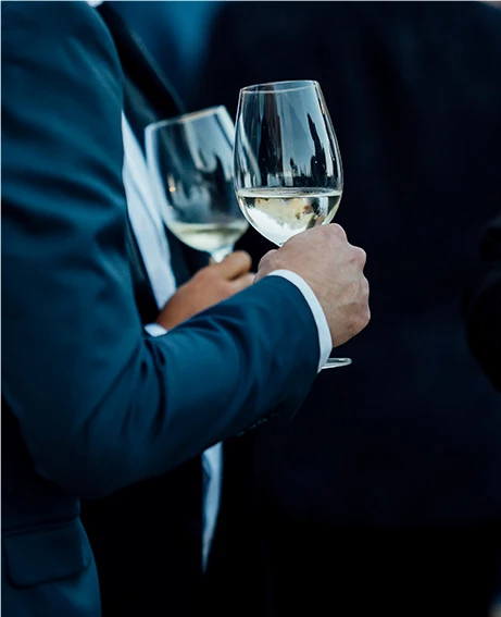 two men in suits holding glasses of white wine