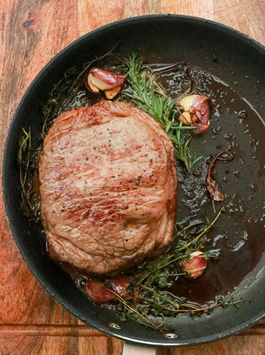 steak being cooked in a fry pan with herbs