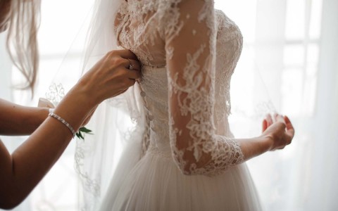 woman closing the back of a bride's lacey dress 