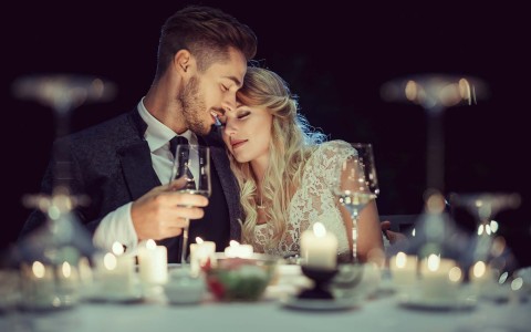 bride and groom at a candlelit table drinking wine