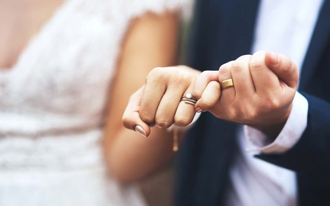 close up of bride and groom intertwining hands with their rings in focus 