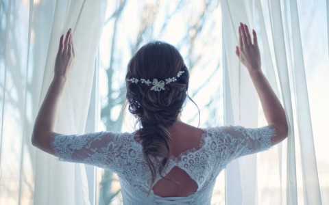 a bride looking out of a window with white curtains