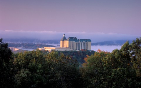 Chateau on the Lake at a distance at sunrise with a purple sky and fog between trees