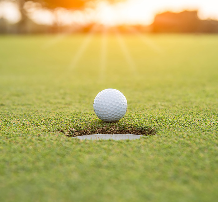 a golf ball about to fall into the hole with sun glare in the background