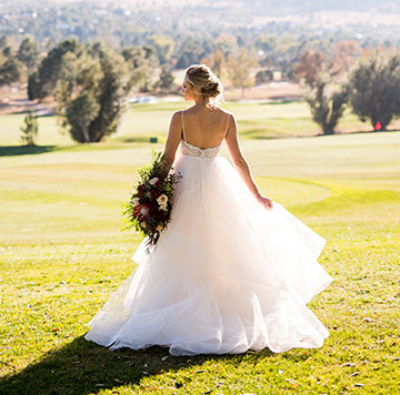 A bride standing on the grass with a bouquet of colorful flowers with her facing toward the mountains in the distance