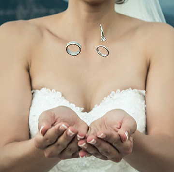 close up of a bride with her hands out catching 3 wedding rings that are falling into her hands