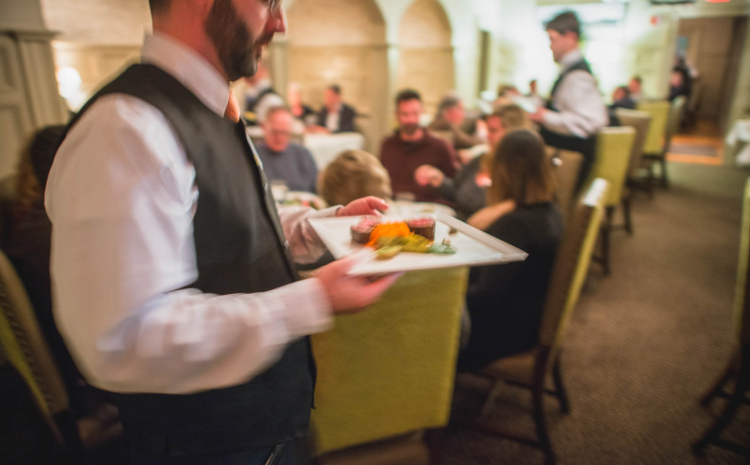Waiter carrying plate of food in full restaurant