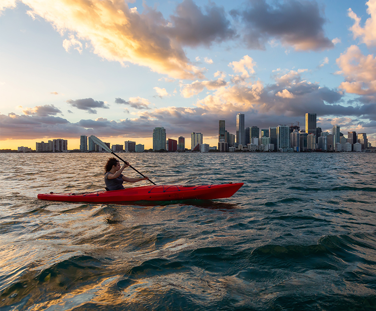 woman kayaking in the ocean with the miami skyline as a backdrop