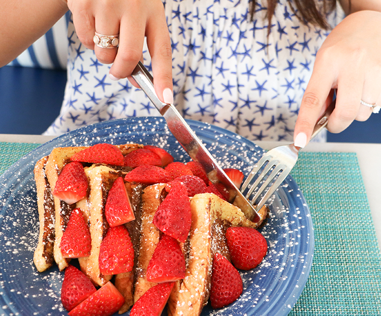 woman cutting into a plate of french toast with strawberries on top