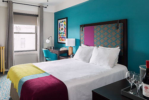 hotel room with blue wall and a bed with a blanket with yellow, blue and maroon