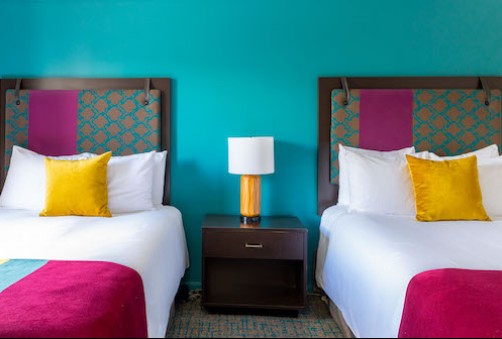 hotel room with blue wall and a bed with a blanket with yellow, blue and maroon