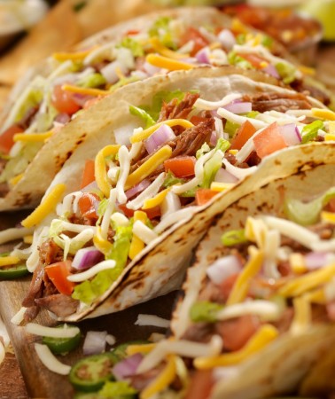 row of tacos garnished with cheese and tomatoes