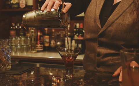 bartender in a grey vest pouring a cocktail