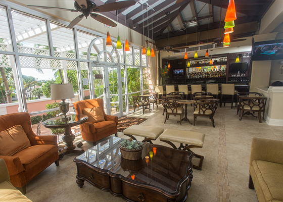 People gathered at hotel seating area next to two women sitting at bar with bartender serving drinks